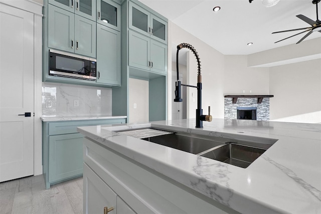 kitchen featuring a fireplace, light stone counters, sink, and light wood-type flooring