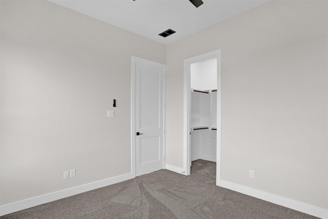 unfurnished bedroom featuring a spacious closet, a closet, ceiling fan, and carpet