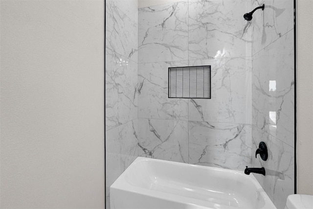 bathroom featuring tiled shower / bath combo and toilet