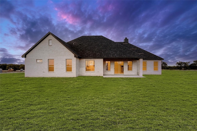 back house at dusk with a lawn and a patio area