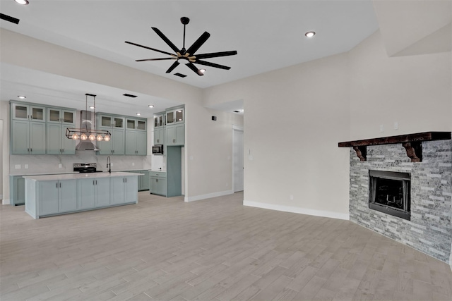 unfurnished living room featuring ceiling fan, sink, light wood-type flooring, and a fireplace