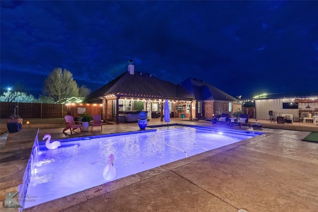 pool at night with a patio, pool water feature, and a jacuzzi