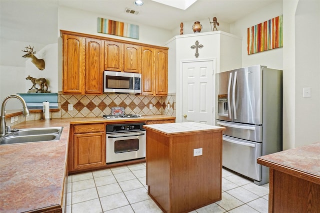 kitchen featuring tasteful backsplash, stainless steel appliances, sink, light tile patterned floors, and a center island