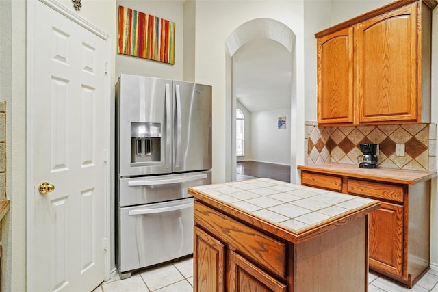 kitchen featuring a center island, backsplash, stainless steel refrigerator with ice dispenser, tile counters, and light tile patterned flooring