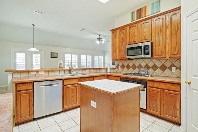 kitchen featuring appliances with stainless steel finishes, tasteful backsplash, light tile patterned floors, a kitchen island, and hanging light fixtures