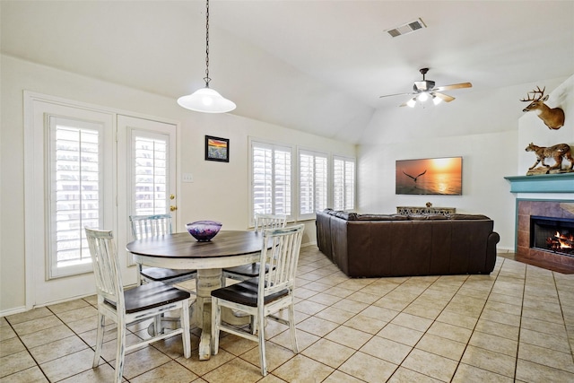 dining area with ceiling fan, a fireplace, light tile patterned floors, and vaulted ceiling