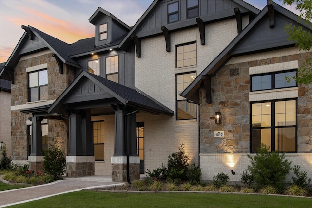 view of front facade featuring stone siding, roof with shingles, board and batten siding, and brick siding