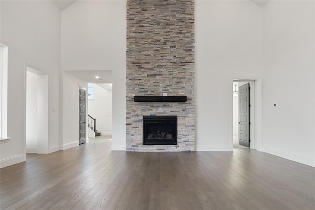 unfurnished living room featuring a towering ceiling, a stone fireplace, baseboards, and wood finished floors