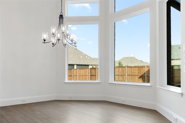 unfurnished dining area with an inviting chandelier, baseboards, and wood finished floors