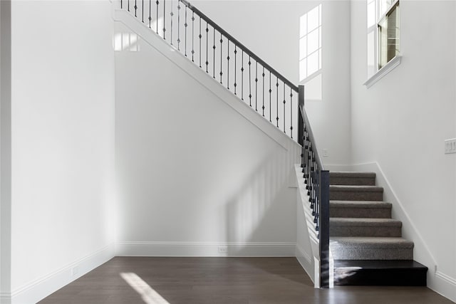 stairway featuring baseboards, a high ceiling, and wood finished floors