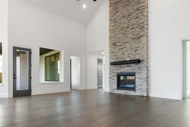 unfurnished living room featuring dark wood-style floors, a stone fireplace, vaulted ceiling, and baseboards