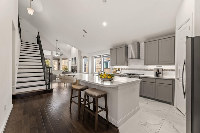 kitchen featuring wall chimney exhaust hood, stainless steel appliances, ceiling fan, a kitchen island, and hanging light fixtures