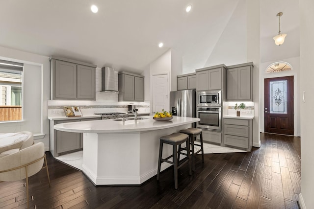 kitchen featuring appliances with stainless steel finishes, sink, wall chimney range hood, high vaulted ceiling, and a breakfast bar area