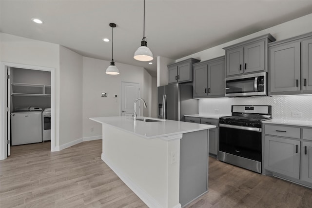 kitchen featuring independent washer and dryer, stainless steel appliances, hanging light fixtures, and a center island with sink