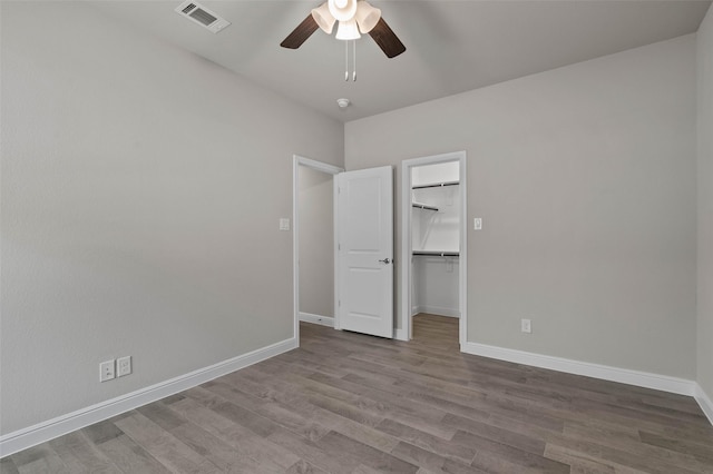 unfurnished bedroom with a walk in closet, a closet, light hardwood / wood-style flooring, and ceiling fan