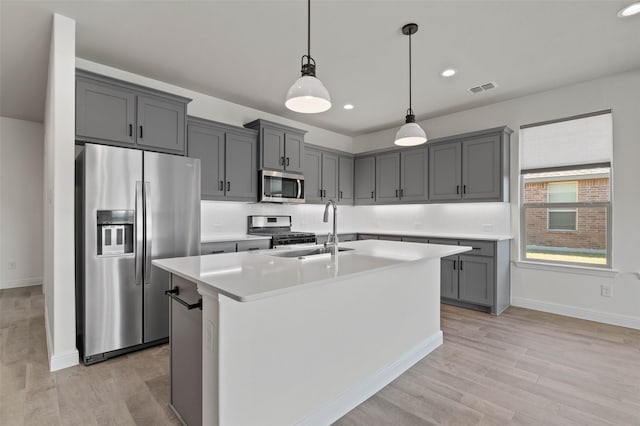 kitchen with gray cabinetry, sink, stainless steel appliances, pendant lighting, and a kitchen island with sink