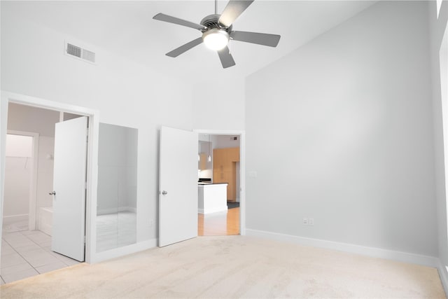 unfurnished bedroom with ensuite bathroom, light colored carpet, ceiling fan, a high ceiling, and a closet