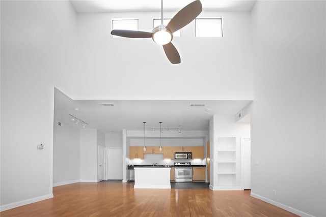 unfurnished living room with ceiling fan, a towering ceiling, and wood-type flooring