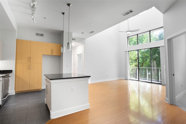 kitchen with ceiling fan, hanging light fixtures, light brown cabinetry, a kitchen island, and range