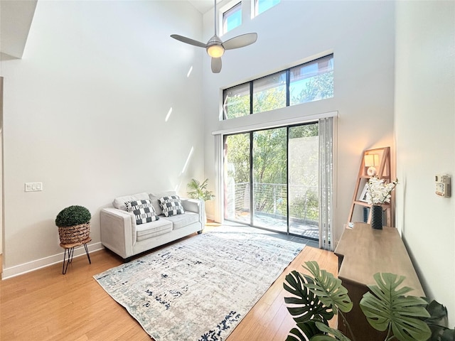 living room featuring ceiling fan, light hardwood / wood-style floors, and a towering ceiling