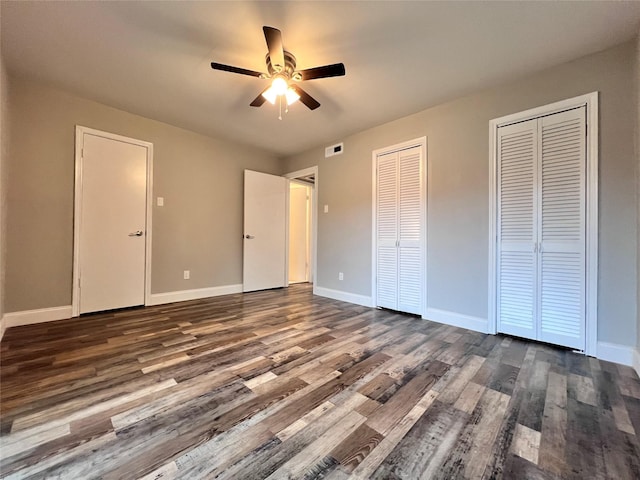 unfurnished bedroom with two closets, ceiling fan, and dark hardwood / wood-style floors