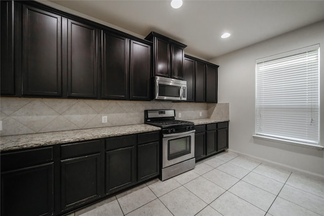 kitchen with light stone countertops, light tile patterned flooring, appliances with stainless steel finishes, and backsplash