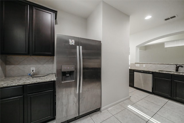 kitchen featuring sink, stainless steel appliances, light stone countertops, light tile patterned flooring, and decorative backsplash