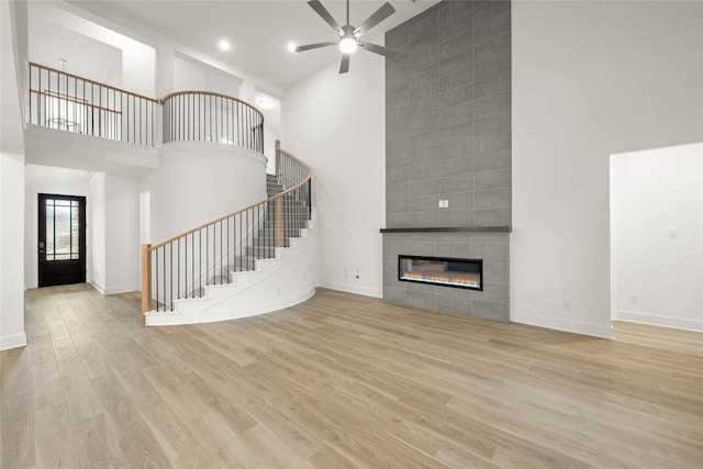 unfurnished living room with a towering ceiling, light hardwood / wood-style floors, a tile fireplace, and ceiling fan