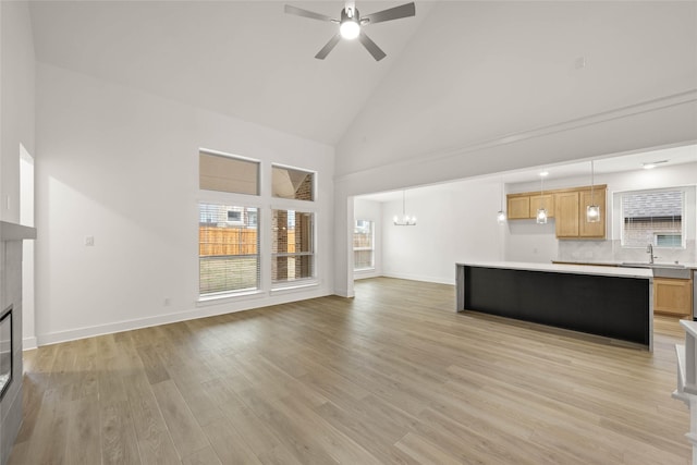 unfurnished living room featuring high vaulted ceiling, sink, ceiling fan with notable chandelier, and light hardwood / wood-style floors