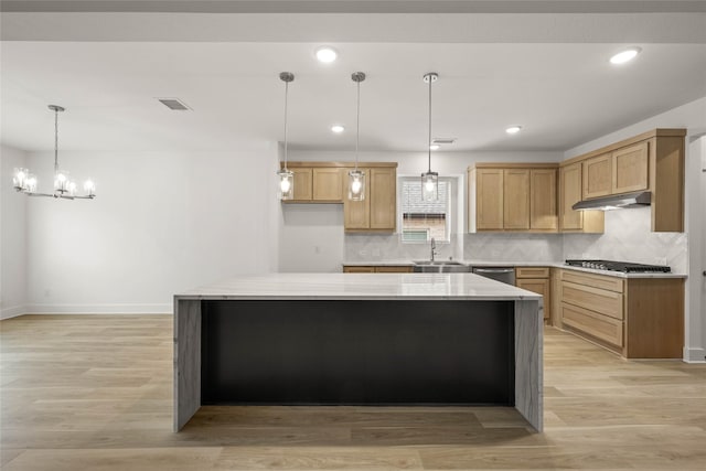 kitchen with appliances with stainless steel finishes, sink, a center island, light stone countertops, and light wood-type flooring