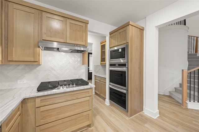 kitchen with stainless steel appliances, backsplash, light brown cabinetry, and light hardwood / wood-style flooring