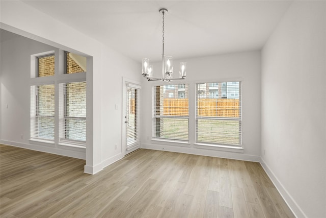 unfurnished dining area with a notable chandelier and light wood-type flooring