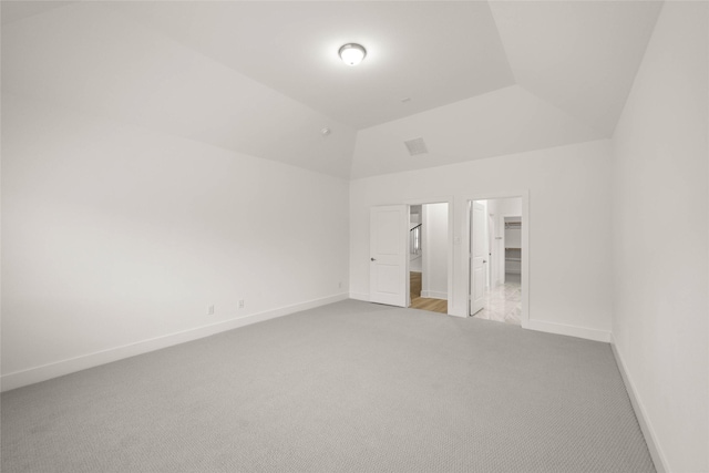 unfurnished bedroom featuring light colored carpet, lofted ceiling, and a walk in closet