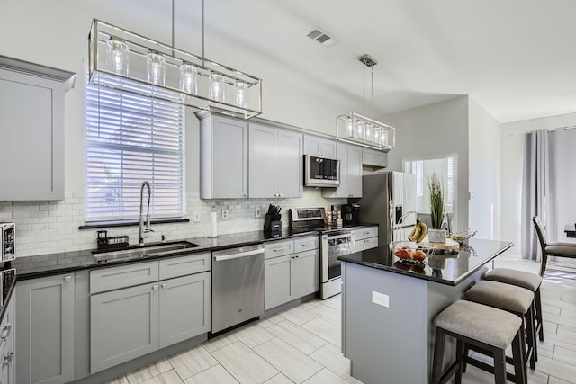 kitchen with sink, stainless steel appliances, backsplash, gray cabinets, and a kitchen island