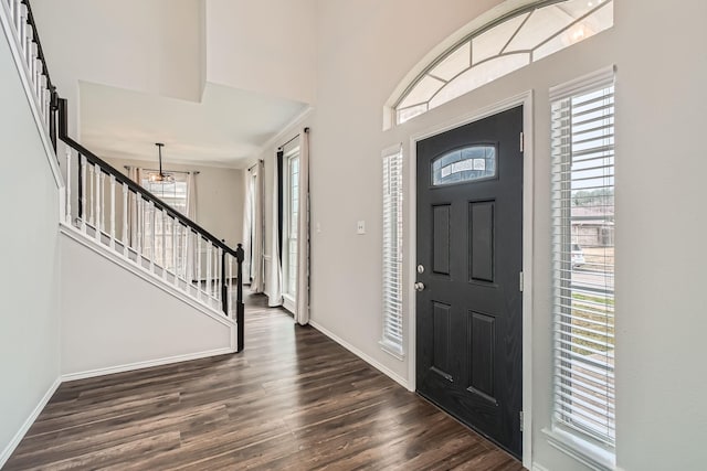 foyer entrance featuring dark wood-type flooring, a towering ceiling, and a notable chandelier