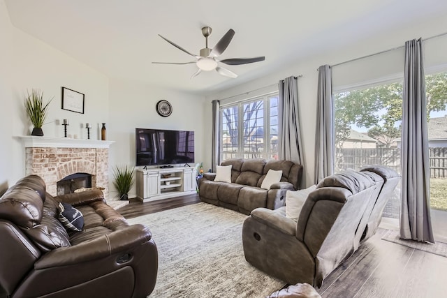 living room featuring ceiling fan, dark hardwood / wood-style flooring, and a brick fireplace