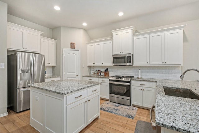 kitchen with sink, appliances with stainless steel finishes, light stone countertops, white cabinets, and a kitchen island