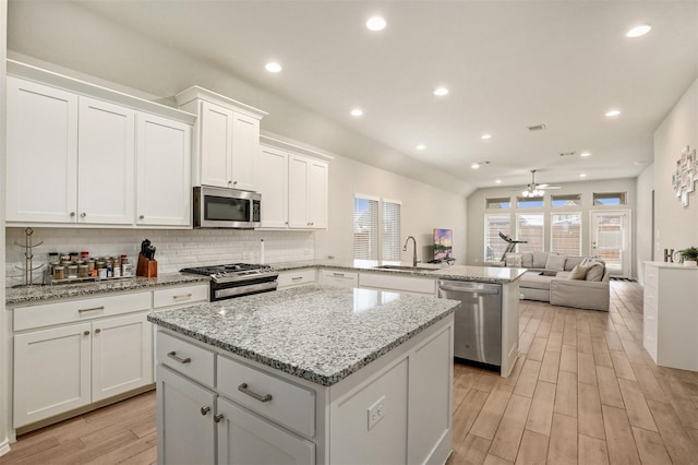 kitchen with sink, a kitchen island, kitchen peninsula, white cabinets, and appliances with stainless steel finishes