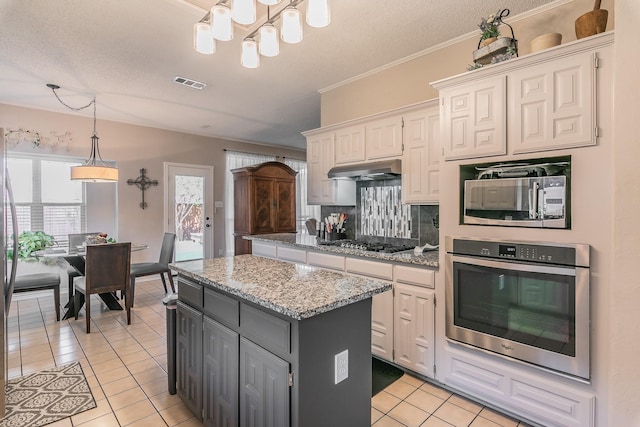 kitchen featuring light stone countertops, appliances with stainless steel finishes, a kitchen island, light tile patterned floors, and white cabinetry