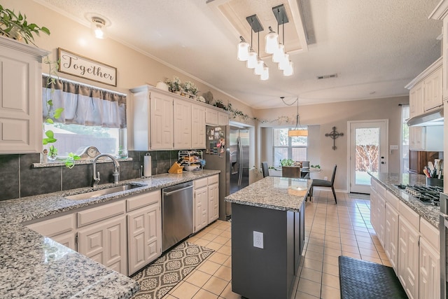 kitchen with light stone countertops, sink, hanging light fixtures, stainless steel appliances, and a kitchen island