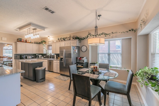 kitchen featuring appliances with stainless steel finishes, decorative light fixtures, a center island, light tile patterned floors, and light stone countertops