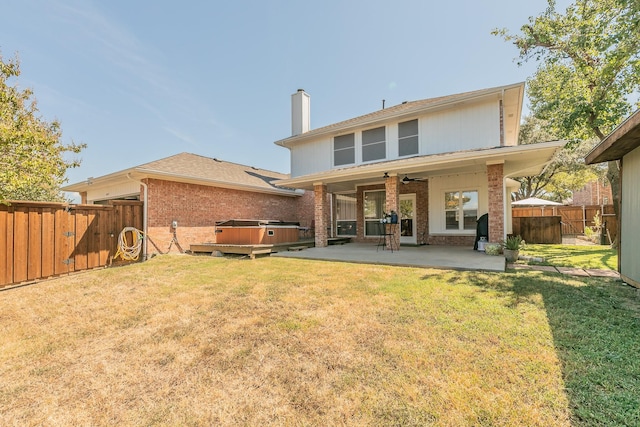 back of house featuring a lawn, ceiling fan, a patio area, and a hot tub