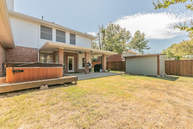 back of house with a hot tub, ceiling fan, a patio area, and a lawn