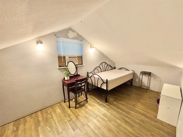 bedroom featuring lofted ceiling, cooling unit, light hardwood / wood-style floors, and a textured ceiling