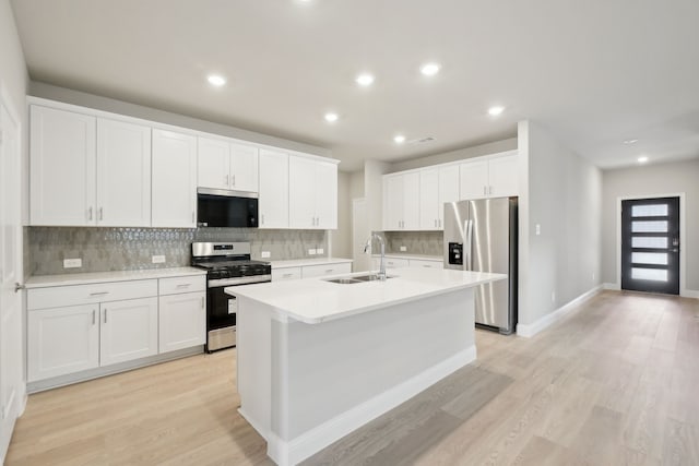 kitchen with white cabinets, appliances with stainless steel finishes, sink, light wood-type flooring, and a center island with sink