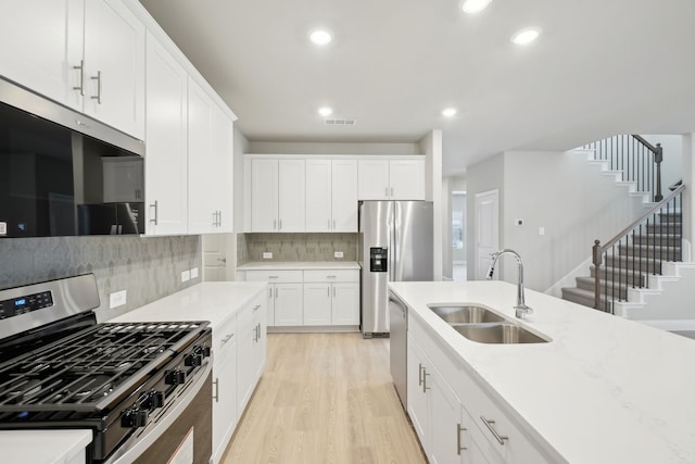 kitchen featuring backsplash, light hardwood / wood-style floors, sink, white cabinetry, and appliances with stainless steel finishes