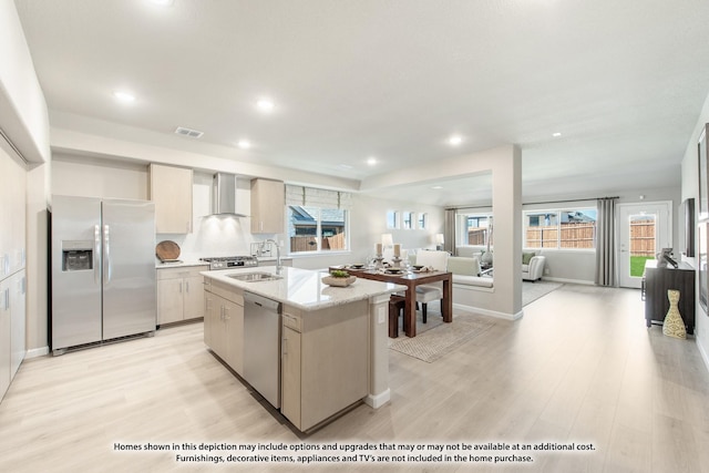 kitchen featuring sink, stainless steel appliances, wall chimney range hood, an island with sink, and light hardwood / wood-style floors