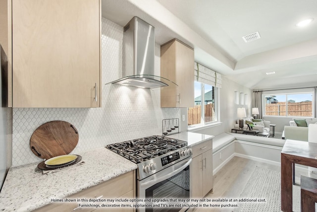 kitchen with stainless steel range, a healthy amount of sunlight, light stone counters, and wall chimney exhaust hood