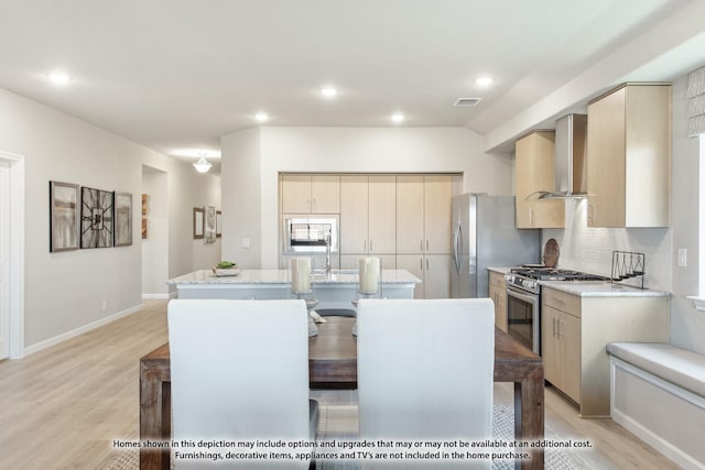 kitchen featuring tasteful backsplash, wall chimney exhaust hood, a kitchen island with sink, light hardwood / wood-style flooring, and stainless steel range with gas cooktop