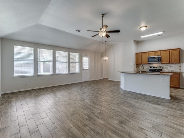 kitchen with ceiling fan, light stone counters, backsplash, lofted ceiling, and appliances with stainless steel finishes